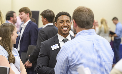 Darius Ramsey in a suit smiling engaged in conversation with a group at UM BAP Meet the Firms 2019